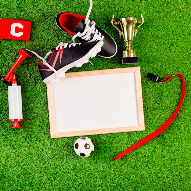 Football Agent concept: Cleats, trophy, whistle, and blank frame on grass with ball and red flag.