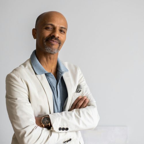 Confident man in a white blazer crosses arms, smiling. Football Agent theme suggested by professional attire.